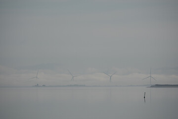 Fjord Landschaft ohne Kontraste - tiefliegende dichte Wolken liegen über Windrädern vor einem See an einem winterlichen Tag