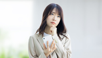 スマホを持って悩む女性・ビジネスウーマン