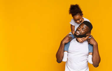 Happy moments. Cute african girl sitting on daddy's shoulders, orange background, empty space