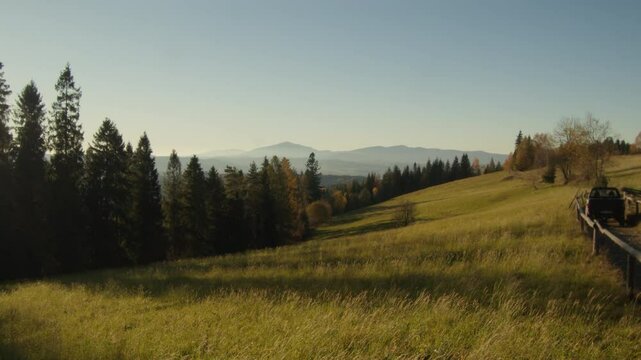Meadow beautifully lighten up by the golden hour of the evening with mountains on the horizon. Brown and dark greens of Polish temperate mixed forest in autumn. High quality 4k footage