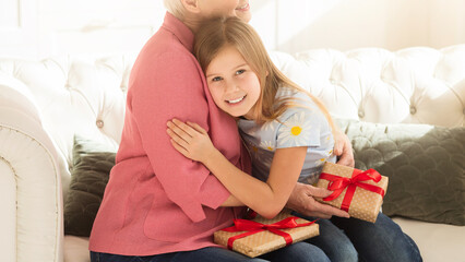 Family holidays. Thankful granny with gifts embracing her grandchild in living room