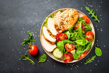 Healthy food. Green salad with grilled chicken meat at black table. Top view.