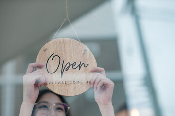 Shopkeeper flipping an open sign at the storefront, signaling the start of the business day.