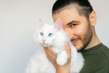 Portrait of young smiling man hugging white fluffy cat with blue eyes on white background.