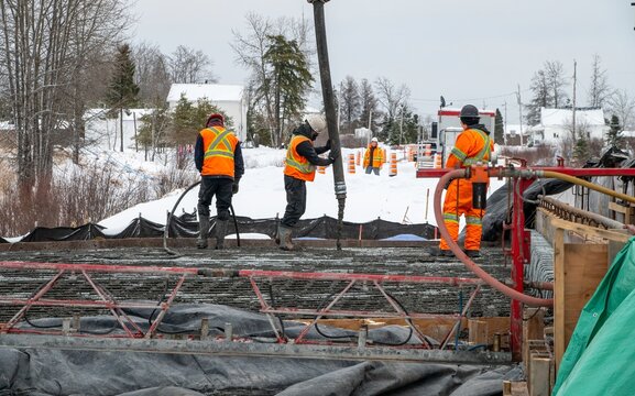 Workers pouring concrete using a concrete pump to build a slab, winter