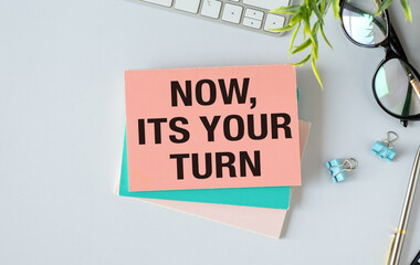 Keyboard, notebook, pen and glasses on blue background , text NOW ITS YOUR TURN.