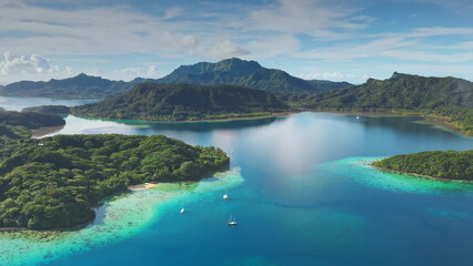 Turquoise water lagoon and green islands with sailboats yachts anchoring near motu in French Polynesia. Remote wild nature tropical paradise, exotic summer luxury travel. Drone aerial panorama shot