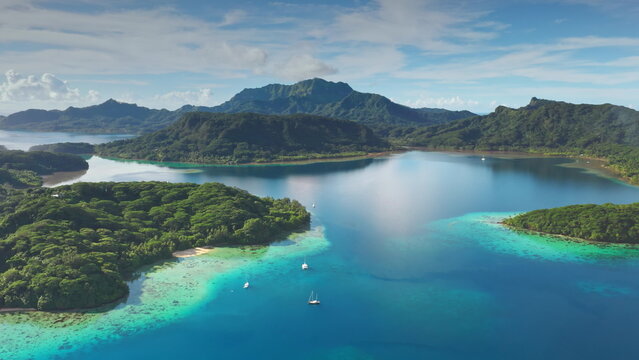 Turquoise water lagoon and green islands with sailboats yachts anchoring near motu in French Polynesia. Remote wild nature tropical paradise, exotic summer luxury travel. Drone aerial panorama shot