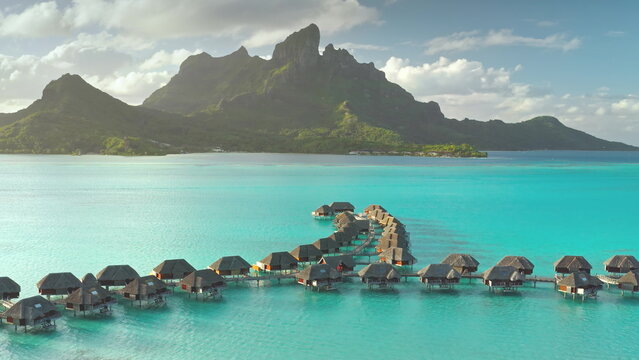 Aerial view overwater bungalows forming line towards mount Otemanu on tropical exotic Bora Bora island, with its turquoise lagoon and lush vegetation. Luxury travel vacation resort in coral reef ocean