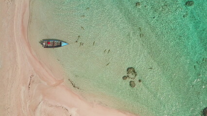 Aerial top down view fishing boat anchored near pink sand beach on tropical island lagoon. Small...