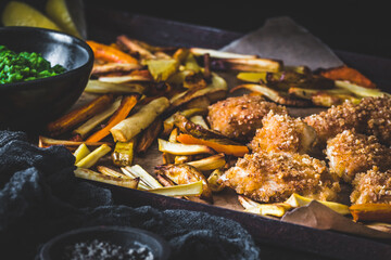Homemade crispy chicken nuggets with vegetable fries made from parsnips, potatoes and carrots, on black background