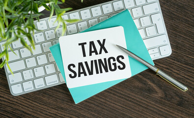 TAX SAVING text on a notebook on keyboard with pen and pencil on grey background