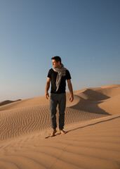 A man stands atop a towering sand dune in the Rub al Khali desert, gazing out over the endless expanse of golden sands. 