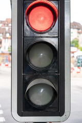 Close up of red traffic light. Behind, in the blurry background, the red white warning markings of a construction site and the houses of the city.