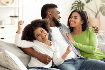 Obraz premium Happy Black Couple Enjoying Spending Time At Home, Hugging And Having Fun Together, Relaxing On Couch In Living Room