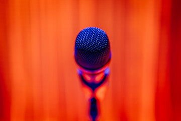Close-up of a microphone in a stand with vibrant orange and blue lighting. Perfect for themes of...