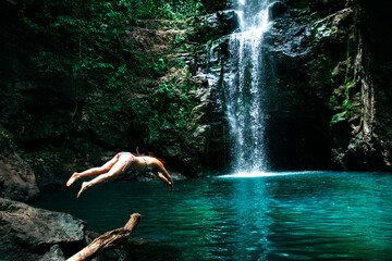 a girl jumping into the water in front of a waterfall