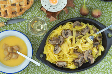 A bowl of pasta with mushrooms and a glass of wine. The table setting is casual and inviting