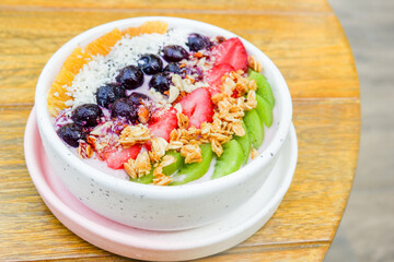 Acai bowl with strawberries, blueberries,orange,kiwi fruit,granola ,chia seeds and coconut flakes on wooden background,close-up, top view, space for text.