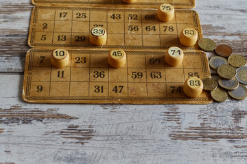 Euro cent coins are placed on old vintage bingo cards and tokens with numbers on a wooden table, old-fashioned