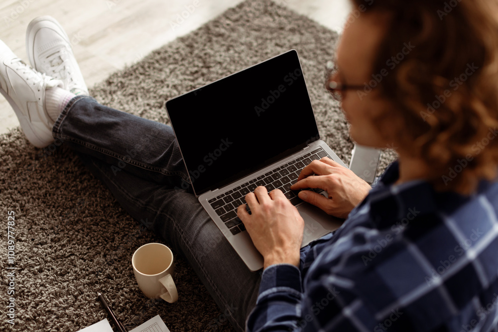 Poster Back-View Of Guy Using Laptop With Blank Screen For Website Advertisement Sitting On Floor At Home. Man Browsing Internet On Computer. Online Technology, Distant Work Concept. Mockup, High Angle Shot