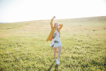 Beautiful blonde woman in summer dress walking in blooming field at sunset
