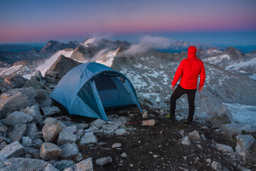 Man watches sunset outside camping tent frome the mountain peak, Valle Camonica, Italian Alps, Lombardy, Italy.	