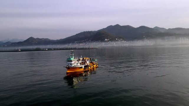 Fishing boat is moving on the sea. A Black Sea region city in the fog in the background