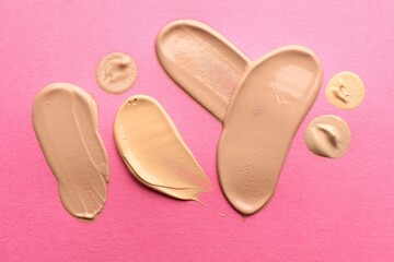 Fototapeta premium Foundation on pink background, top view. Smears of cosmetic product