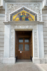 Obraz premium Trieste, Italy - June 27, 2024: Serbian Orthodox Church of Saint Spyridon. Entrance wooden door set in monumental sculpted frame with golden icon and image of Saint Michael, the archangel
