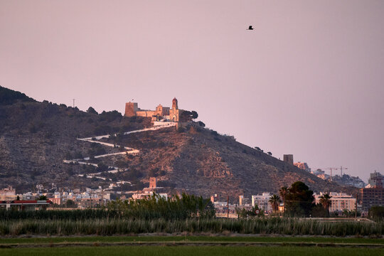 Basking in the warm hues of a summer sunset, Cullera Castle stands majestically atop Cullera Mountain, overlooking the vibrant life below.