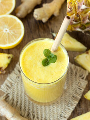 Yellow pineapple ginger lemon smoothie with fresh mint on wooden table. Top view. Healthy homemade...