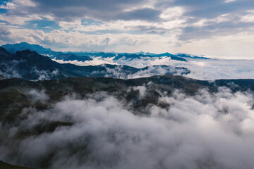 Fototapeta premium Serene mountain scenery with dense fog at the high peak in the early morning and a layered mist under the low cloudy sky.