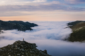 Man reaching the summit. Walking on the mountain at sunrise. Person watching the view above the clouds. Drone shot.