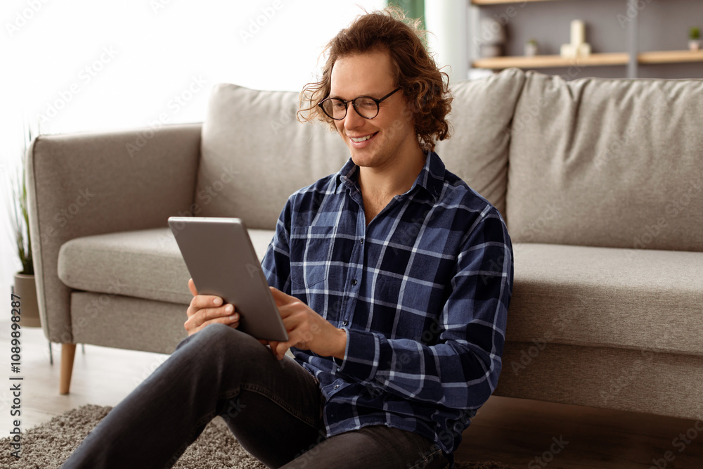 Aufkleber happy millennial man using digital tablet browsing internet sitting on floor in living room at home.
