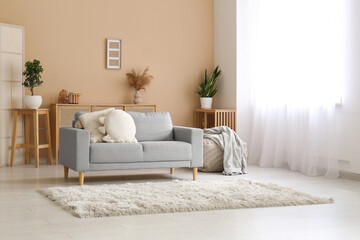 Fototapeta premium Cozy sofa with pillow, pouf with plaid and carpet in interior of living room