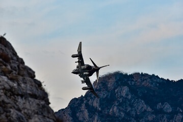 A dynamic photograph of a two engine  fighter jet soaring through the sky with its afterburners glowing brightly. The aircraft is captured from below, highlighting its powerful and aggressive stance 