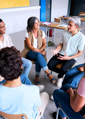 Vertical. Diverse happy group of high school students sitting on chairs in circle interacting during lesson. Multiracial adolescents talking together to classmates and female teacher in support class