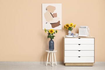 Chest of drawers, stool and vases with beautiful sunflowers in interior of living room