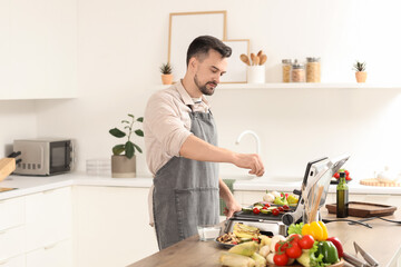 Young man adding salt onto tasty vegetables skewers on modern electric grill in kitchen