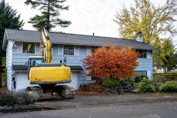 Heavy duty excavator equipment parked in a driveway of a house ready to be torn down, fall...