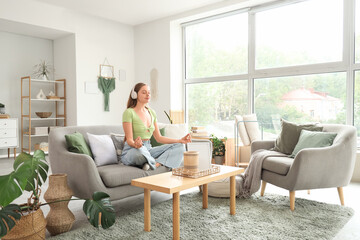 Fototapeta premium Young pretty woman in headphones meditating on sofa in stylish living room