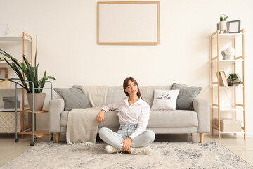 Young woman sitting on carpet near grey sofa in living room