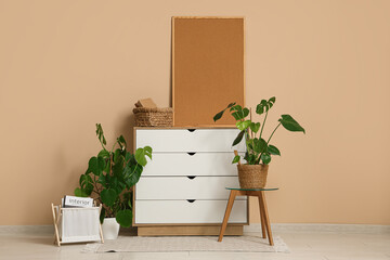 Chest of drawers, houseplants and frame near beige wall
