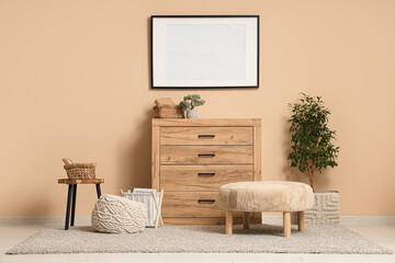 Chest of drawers, poufs, decorative tree and frame on beige wall in room