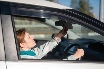 Caucasian woman sitting behind the wheel and looking in the mirror. 