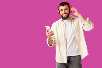 Fototapeta premium Handsome young happy man in headphones with mobile phone on purple background
