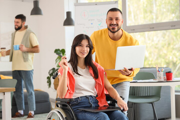Female designer in wheelchair with graphic tablet and her colleague working at office