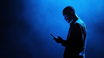 Silhouette of a young man using his phone in blue light.