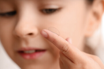 Cute little girl putting in contact lens, closeup